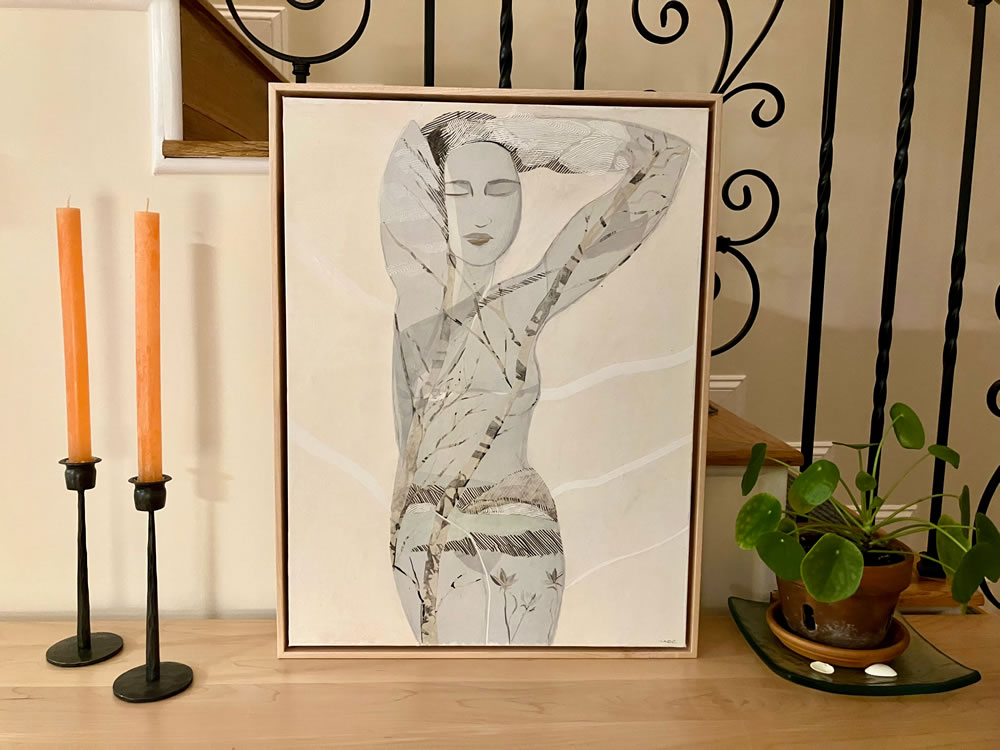 The piece Winter Meditation framed and sitting on a table with candles and a plant while leaning against a stair railing.